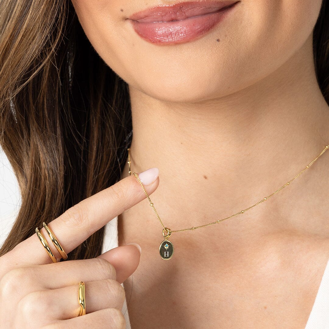 Close-up of a person wearing a gold necklace with a pendant, holding their finger up.