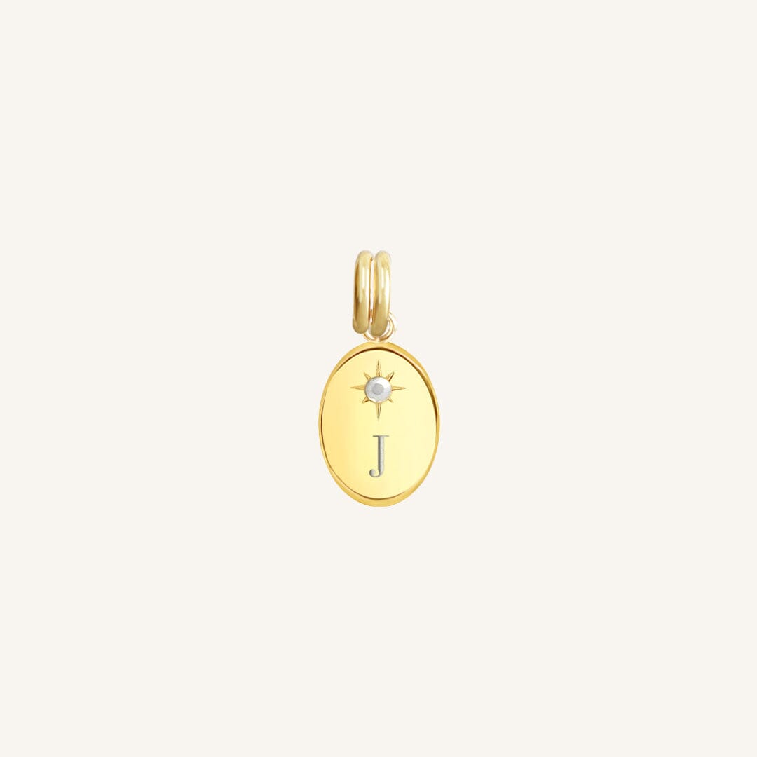 Gold pendant with letter 'J' on a light beige background