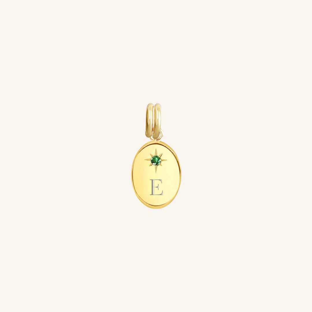 Gold pendant with a green gemstone and letter 'E' on a light beige background
