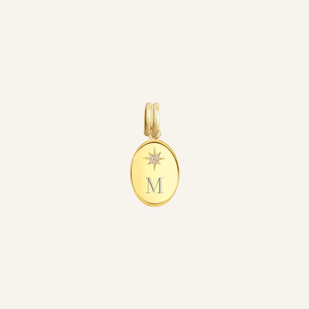 Gold pendant with 'M' letter on a light beige background