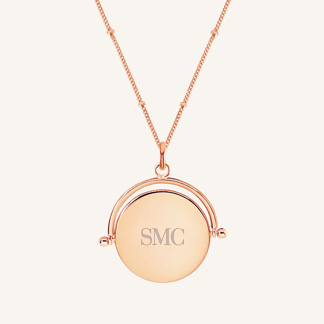 A rose-coloured pendant with the initials engraved on it, featuring a spinning mechanism, on gold chain