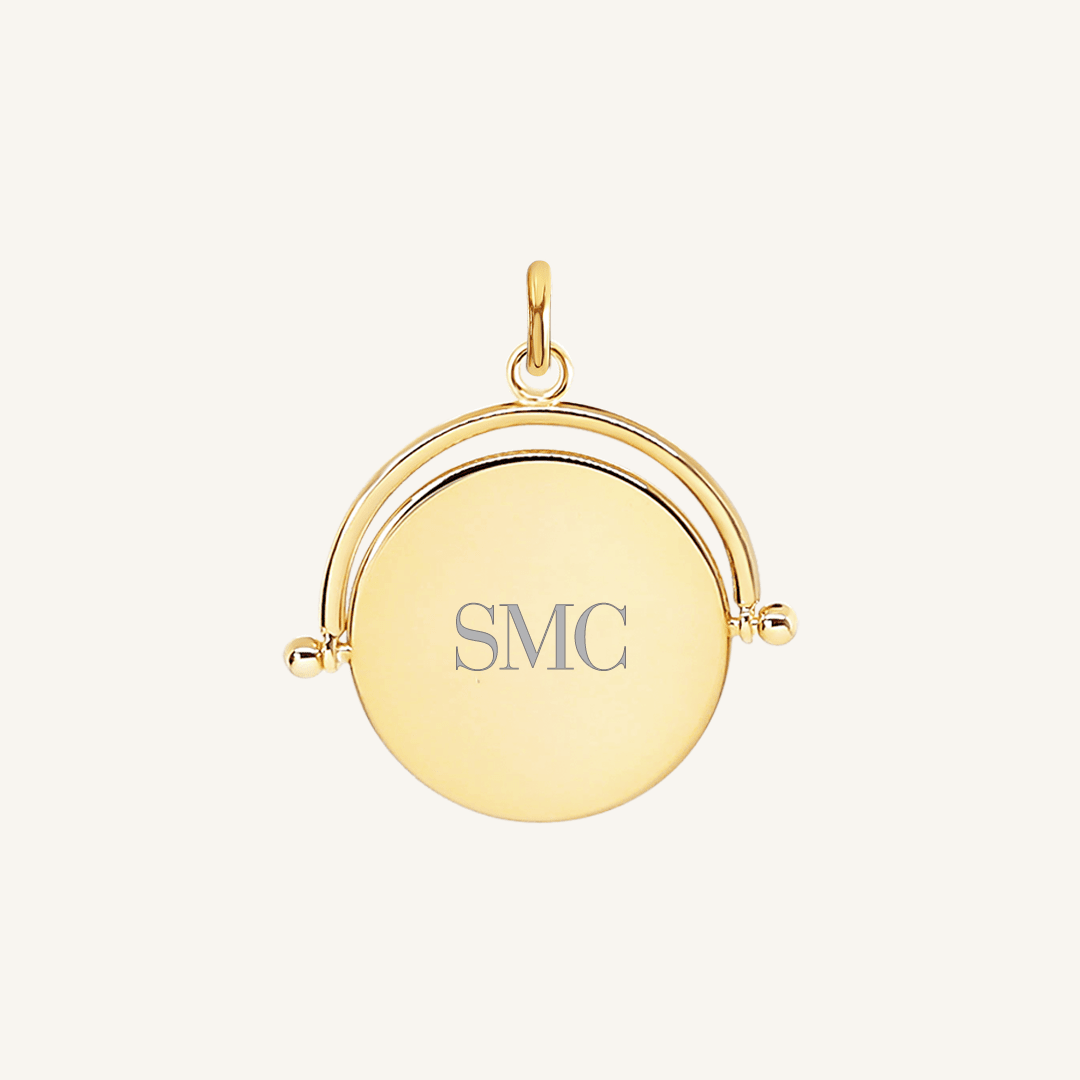 A gold-coloured pendant with the initials engraved on it, featuring a spinning mechanism.