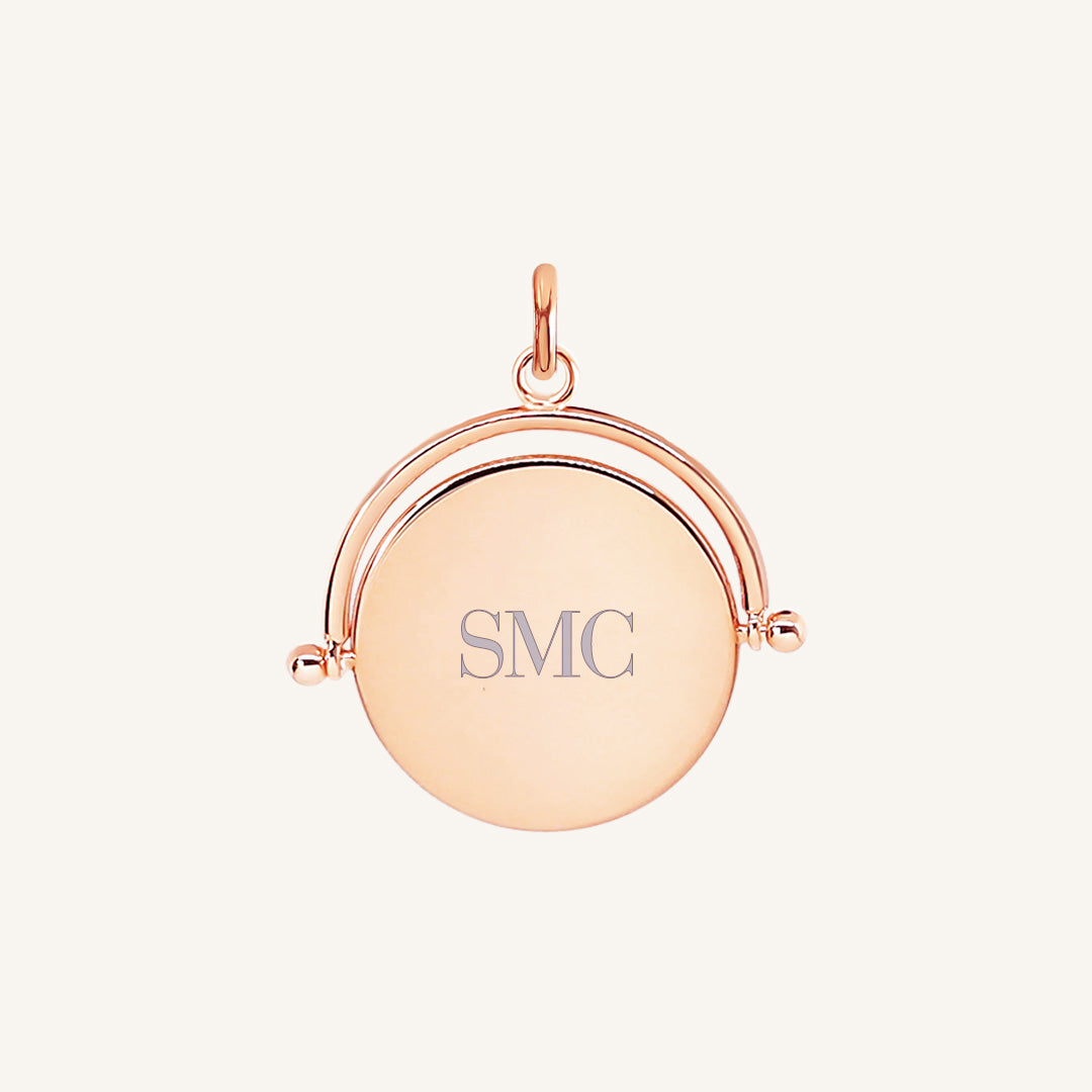 A rose-coloured pendant with the initials engraved on it, featuring a spinning mechanism.