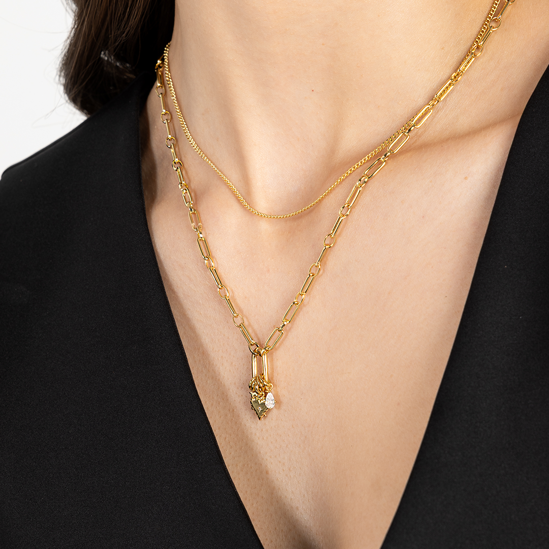 A delicate heart-shaped charm in gold metal tone worn on link chain close up on neck