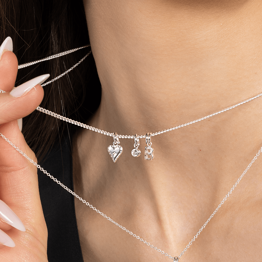 A delicate heart-shaped charm in gold metal tone worn on plain chain close up on neck