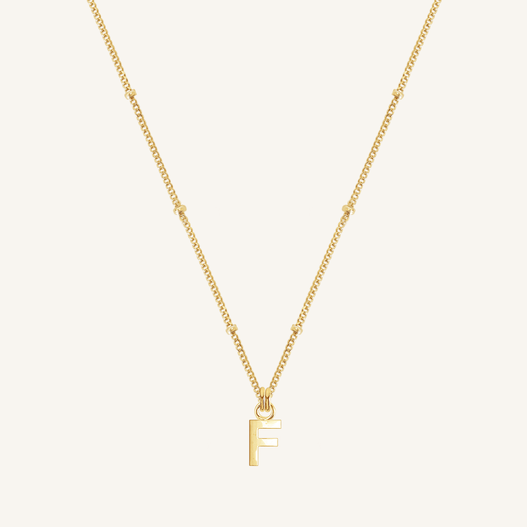Gold necklace with a 'F' pendant on a light beige background