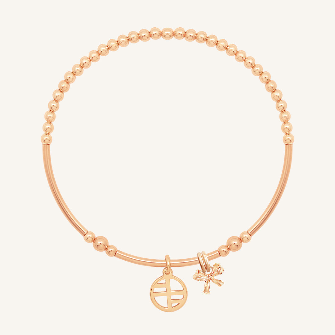 A rose-tone metal bracelet with a beaded design, featuring a charm in the shape of a bow