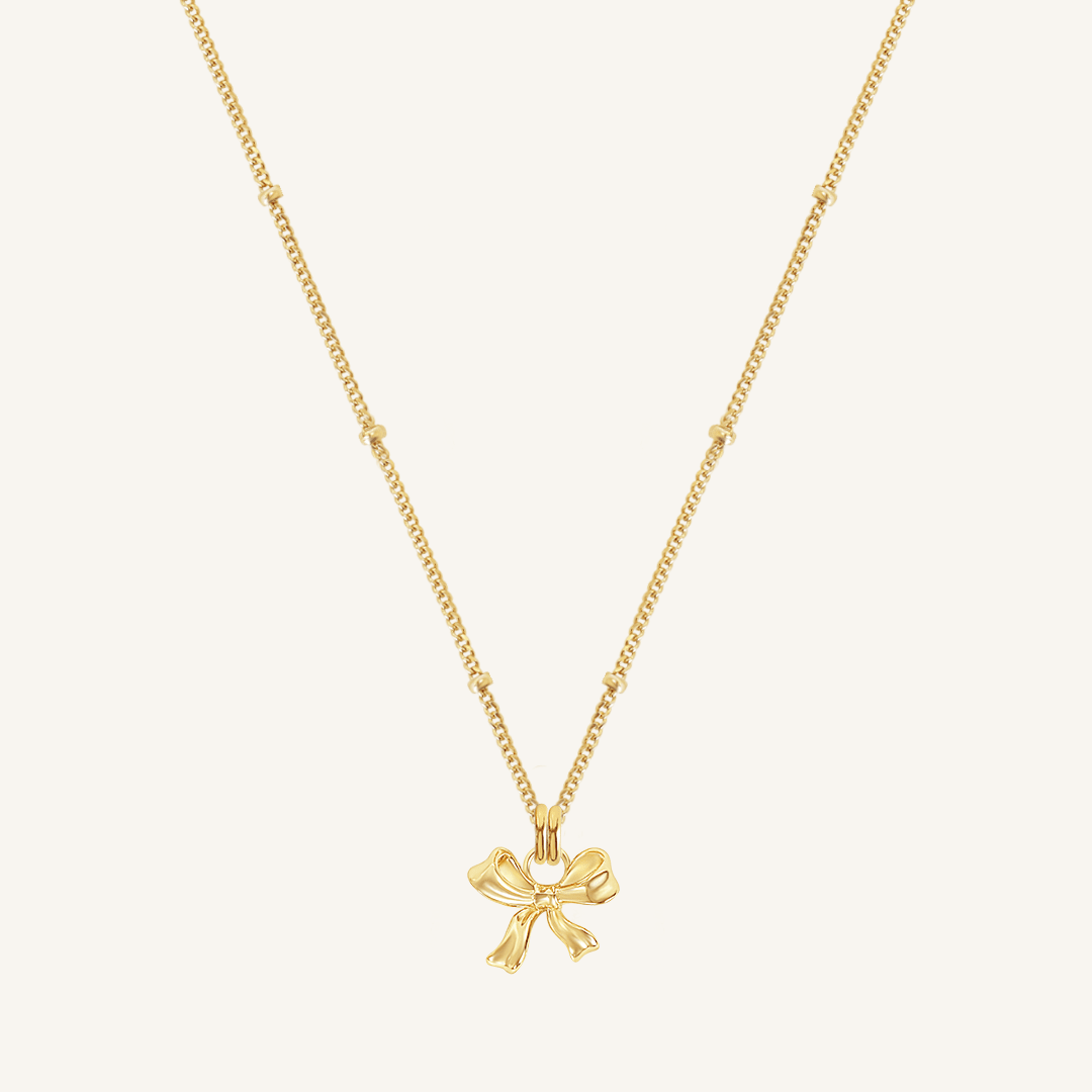 A gold-colored necklace featuring a bow-shaped charm attached to a hoop.