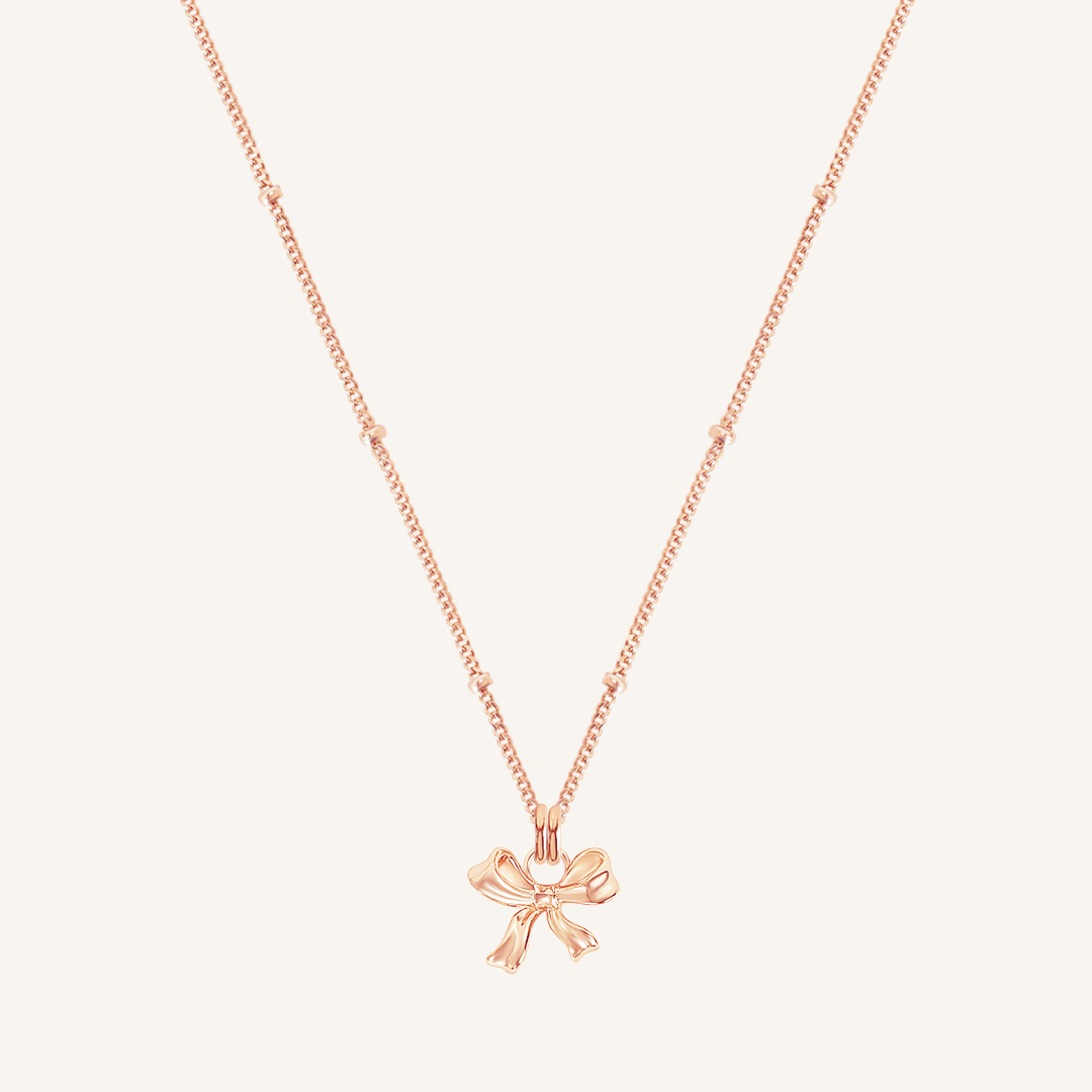 A rose-colored necklace featuring a bow-shaped charm attached to a hoop.