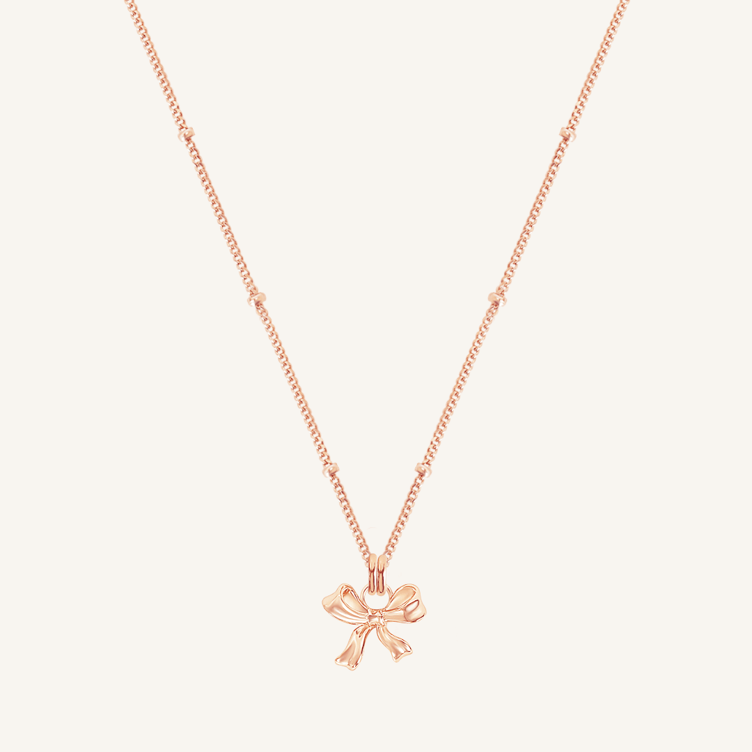 A rose-colored necklace featuring a bow-shaped charm attached to a hoop.
