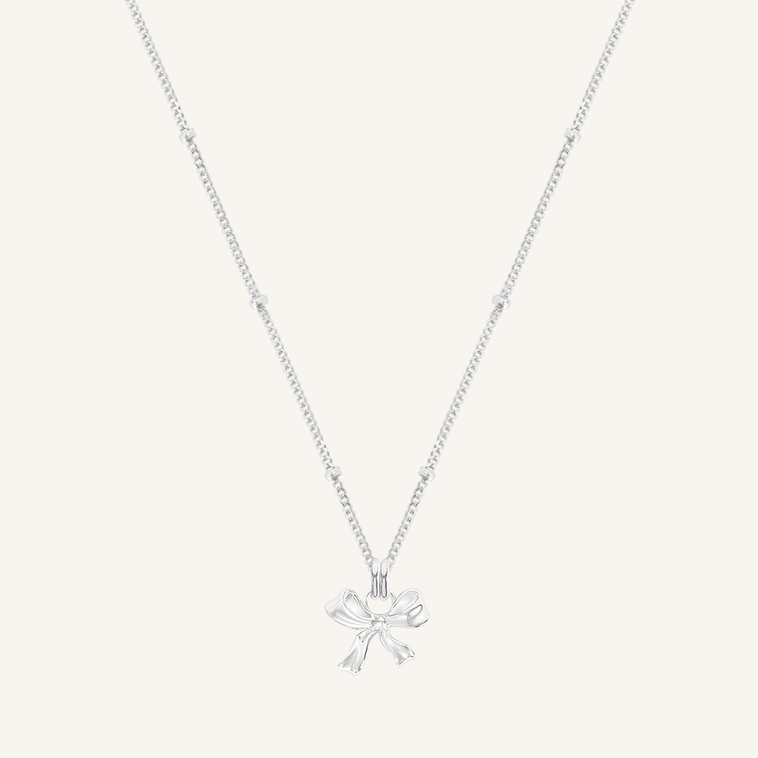 A silver-colored necklace featuring a bow-shaped charm attached to a hoop.
