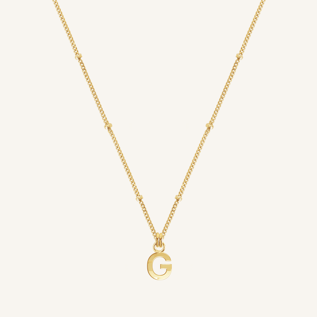 Gold necklace with a 'G' pendant on a light beige background