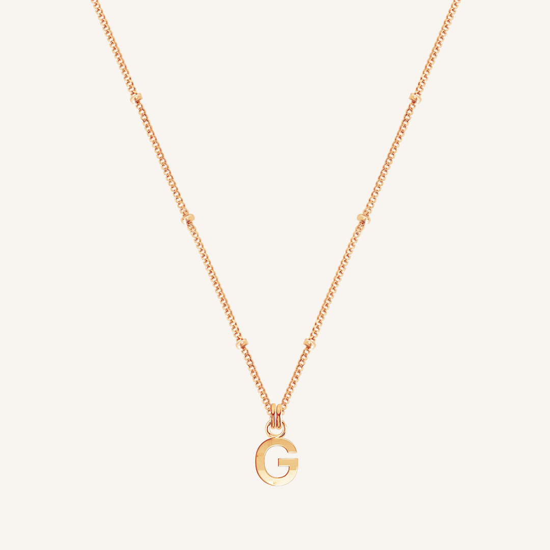 Gold necklace with a 'G' pendant on a light beige background