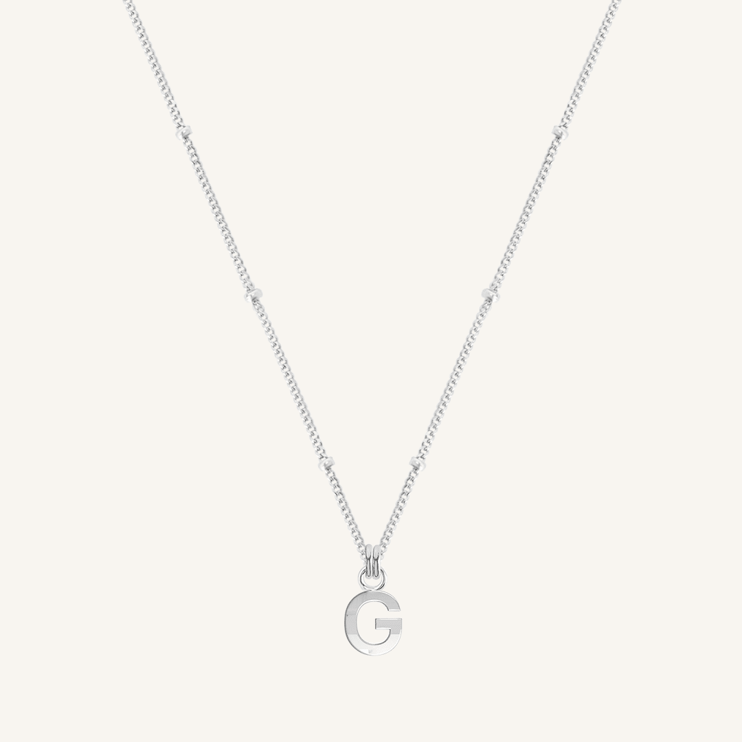 Silver necklace with a letter 'G' pendant on a light gray background
