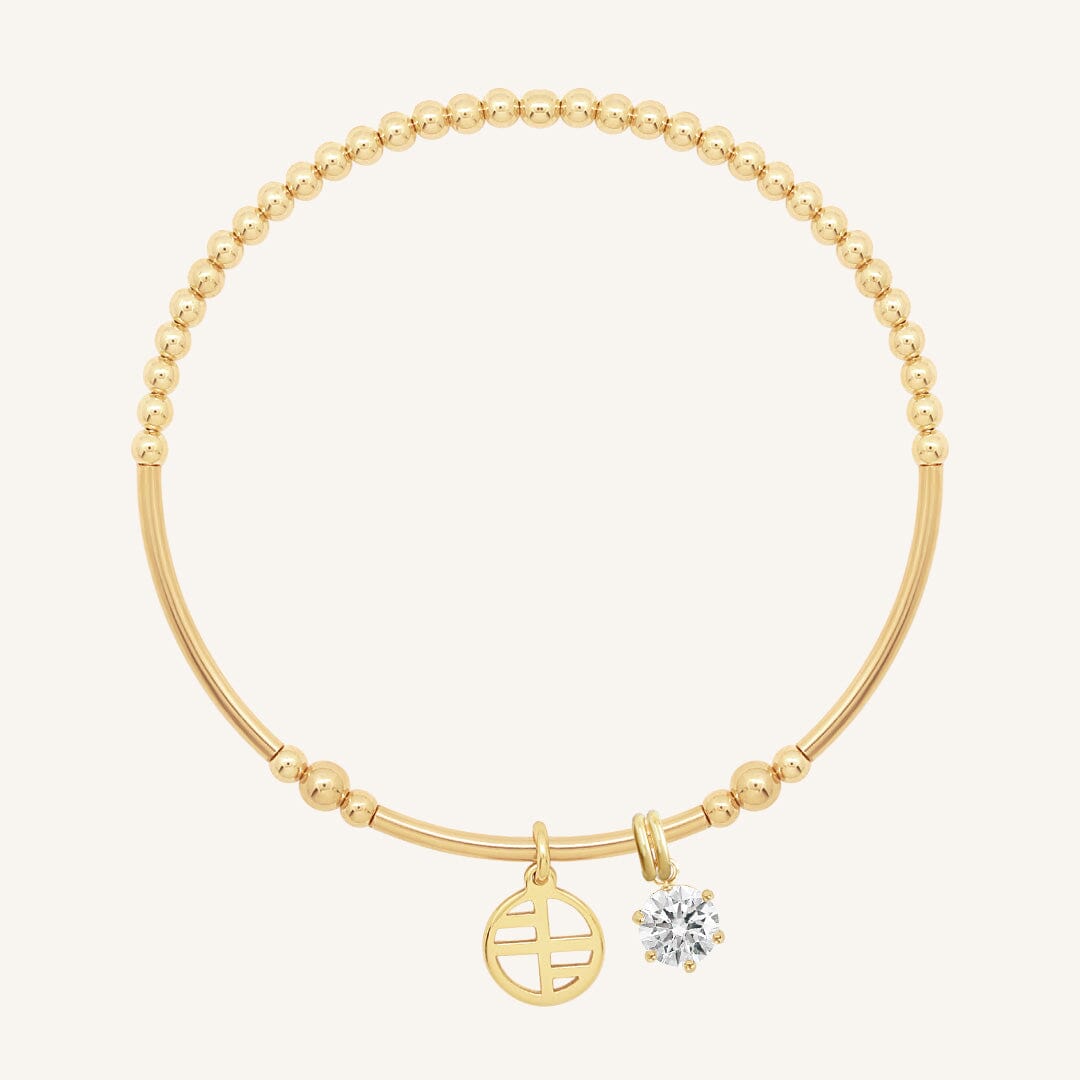 A gold-tone charm bracelet with a beaded design and two charms, one circular and one in the shape of a heart with a small cubic zirconia inside.