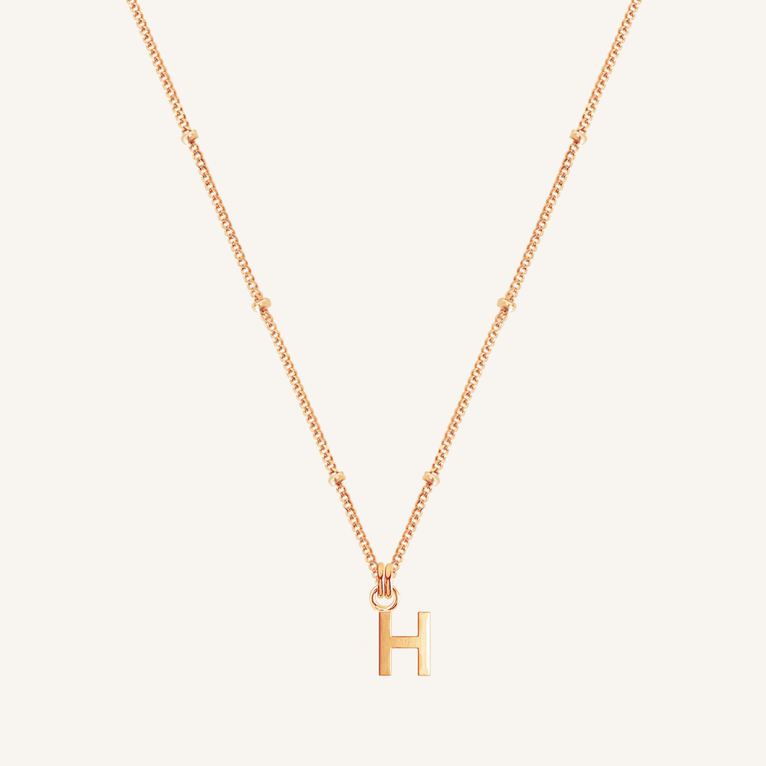 Gold necklace with 'H' pendant on a light beige background