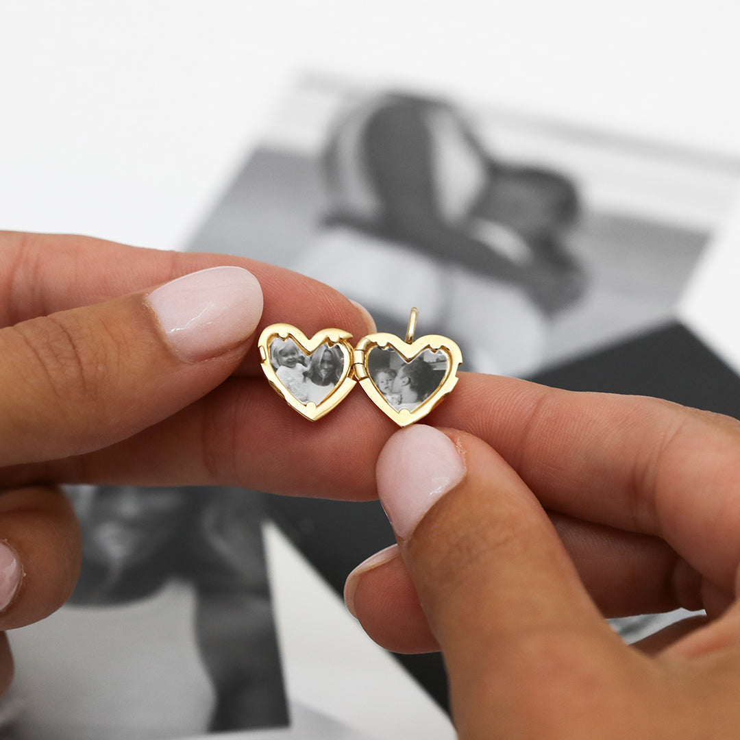 A gold heart-shaped photo locket open to show photos inside, held by model