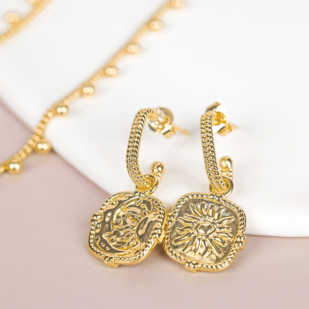 Gold earrings with intricate designs on a light background