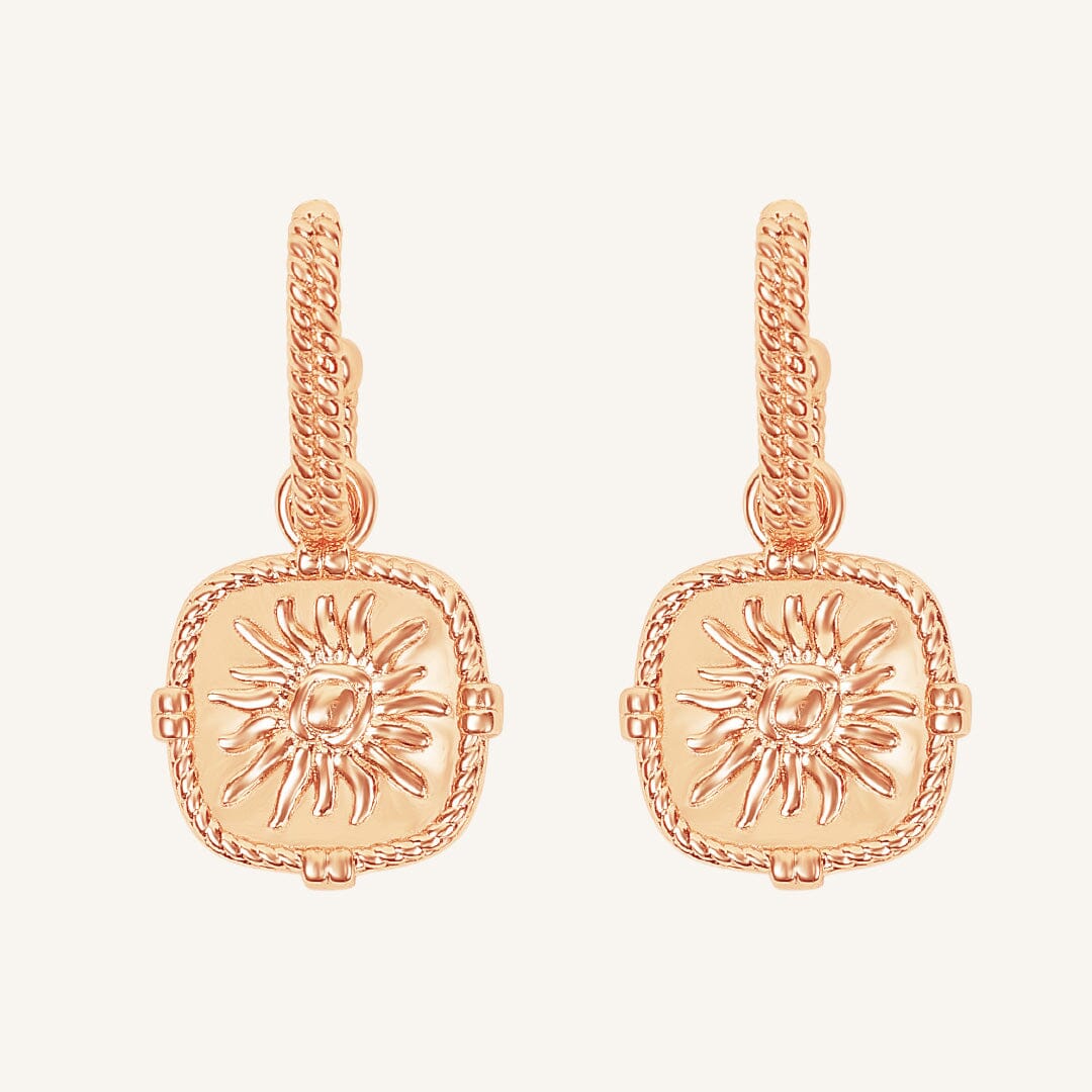 Rose gold earrings with sun design on a light pink background