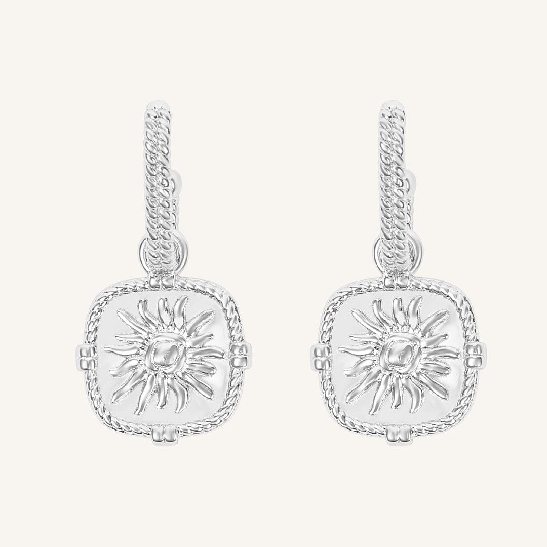 Pair of silver earrings with sun design on a white background