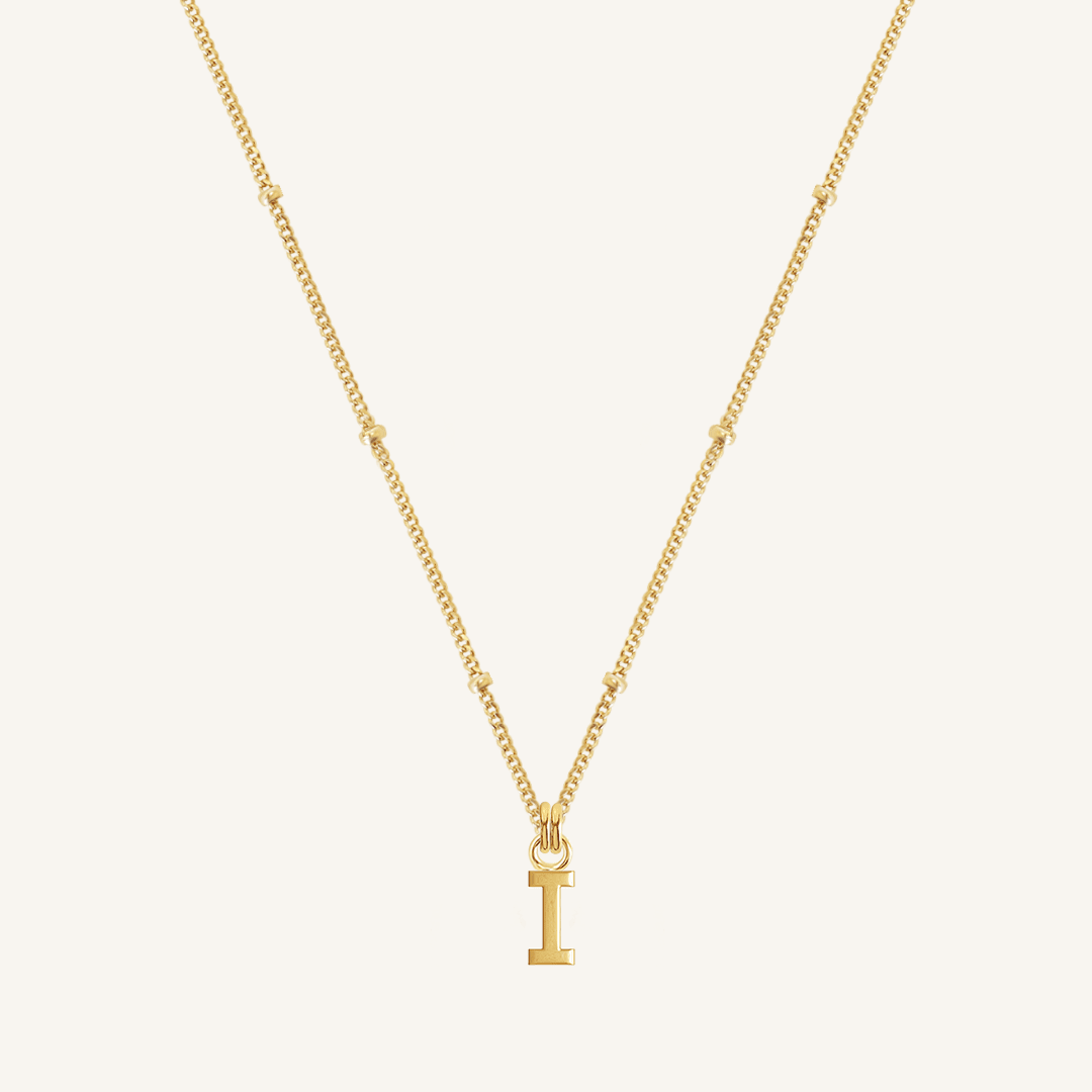 Gold necklace with a 'I' pendant on a light beige background