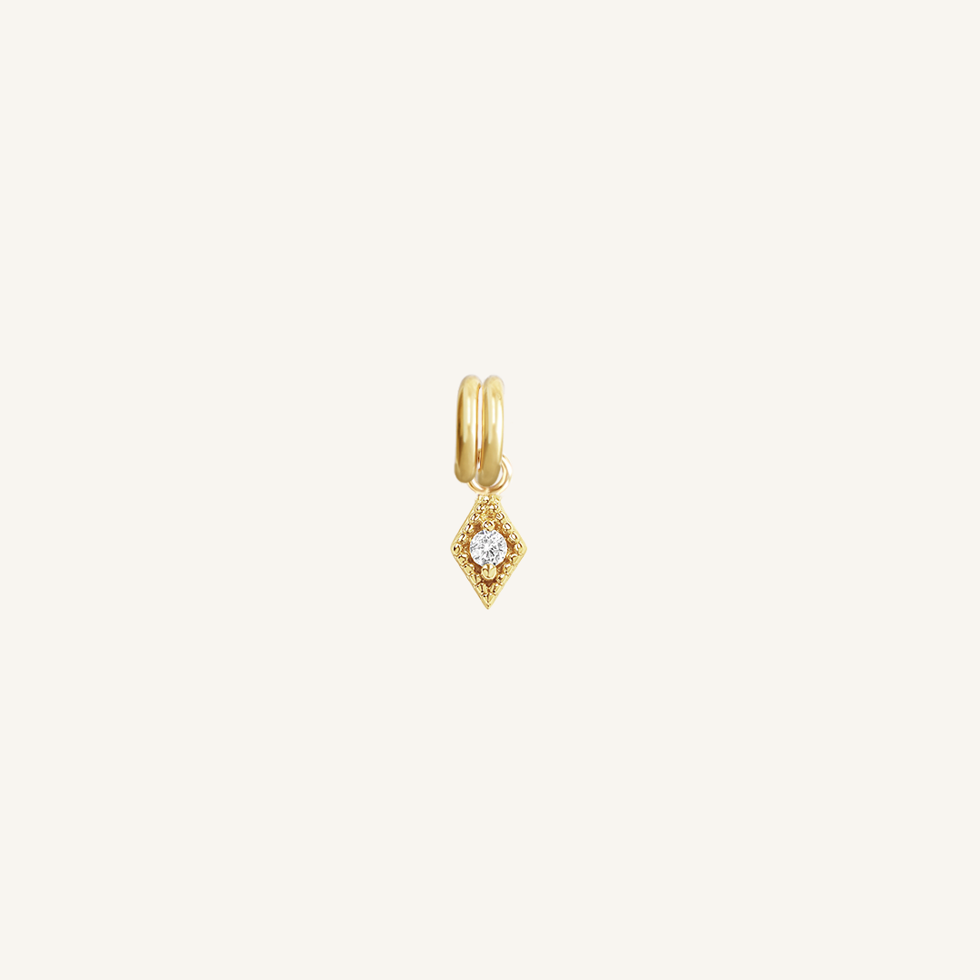A small, diamond-shaped gold charm with a white stone in the center, isolated on a white background.