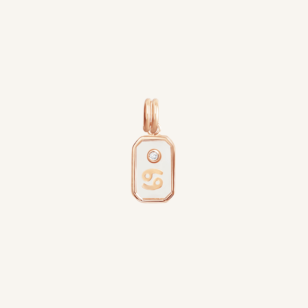 A rose gold rectangular shaped charm with the Cancer zodiac symbol on it, designed with an iridescent finish.