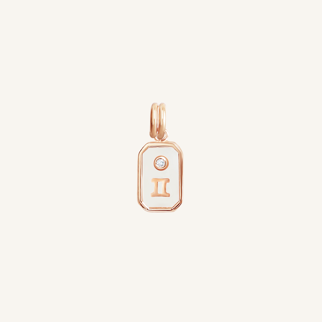 A rose gold rectangular shaped charm with the Gemini zodiac symbol on it, designed with an iridescent finish.