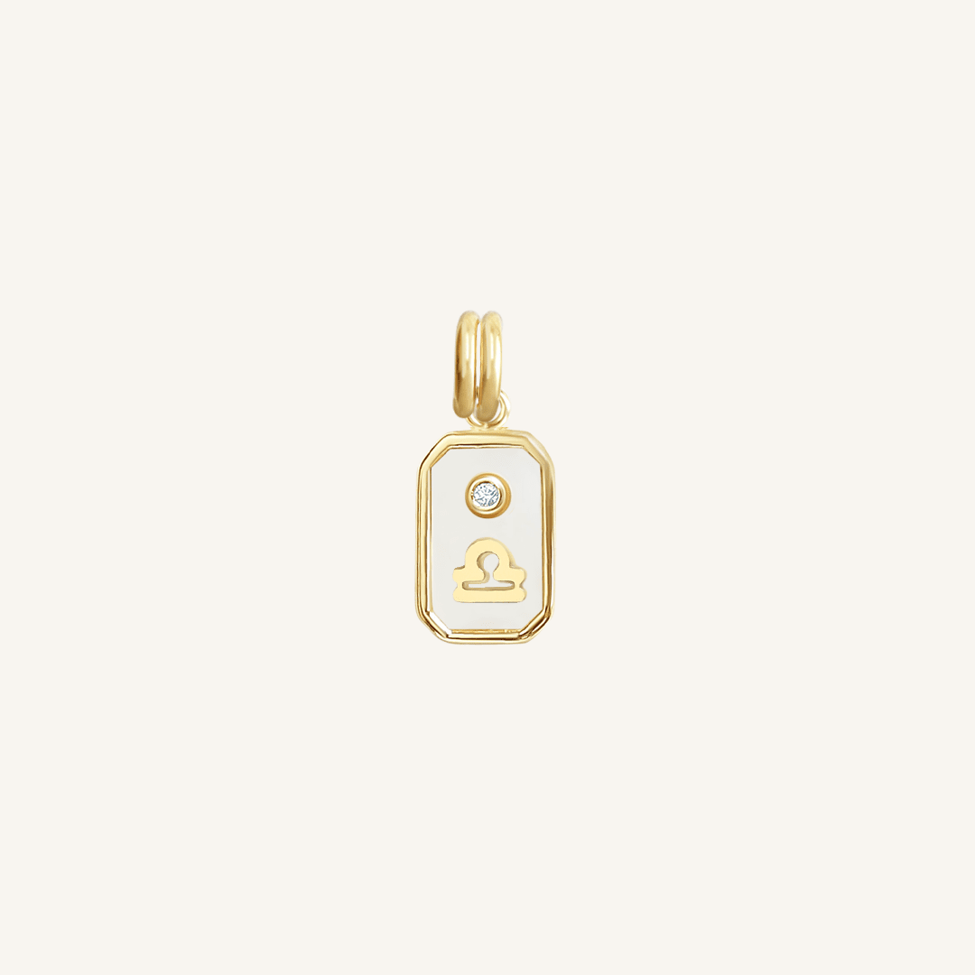 A gold rectangular shaped charm with the Libra zodiac symbol on it, designed with an iridescent finish.