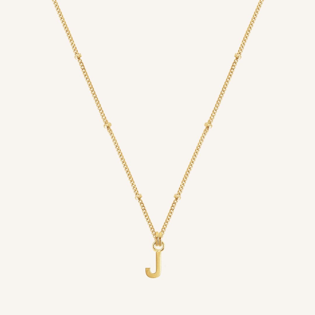 Gold necklace with a 'J' pendant on a light beige background