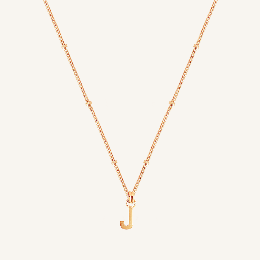 Rose gold necklace with a 'J' pendant on a light beige background