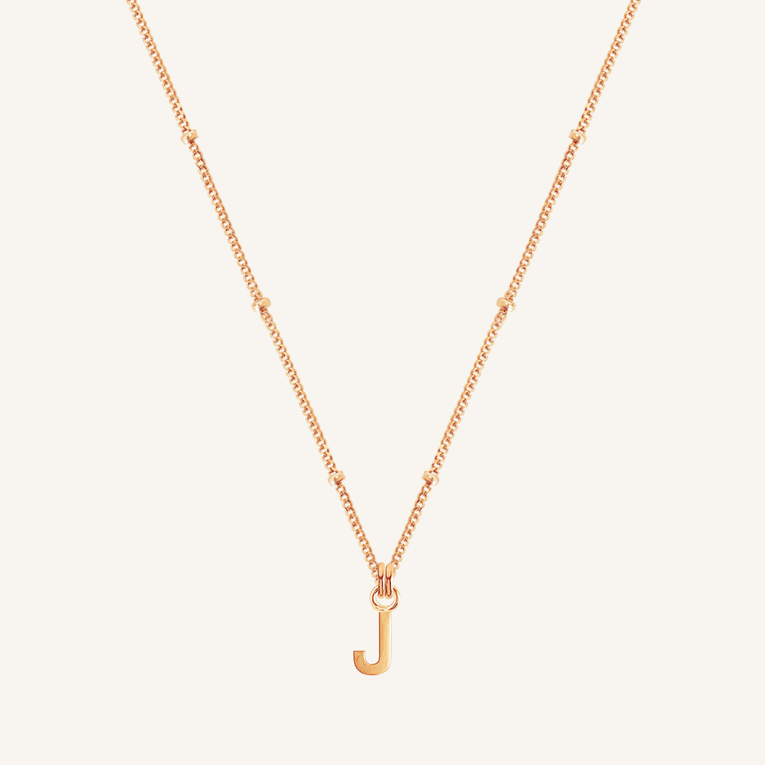 Rose gold necklace with a 'J' pendant on a light beige background