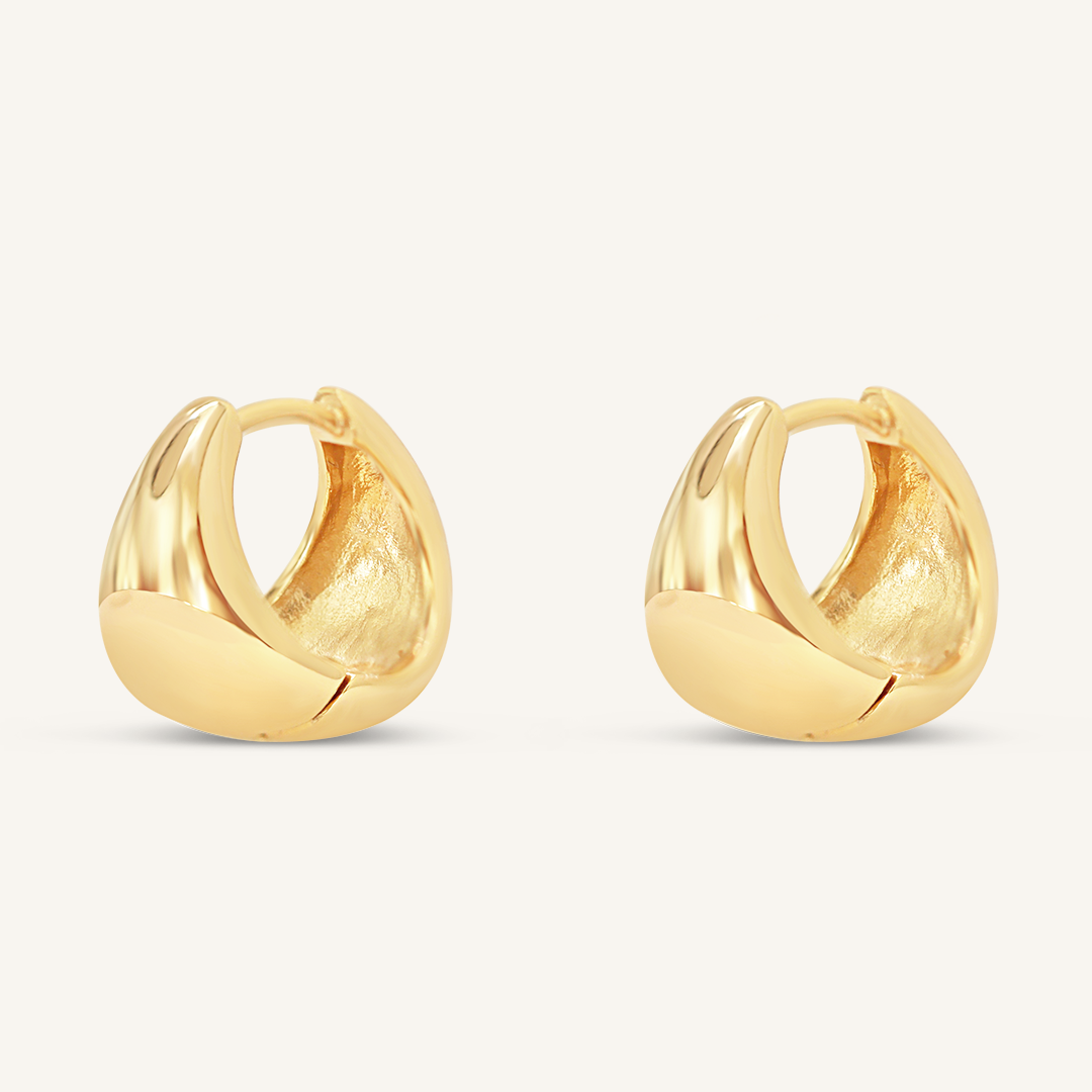 A pair of gold-colored huggie hoop earrings on a white background.