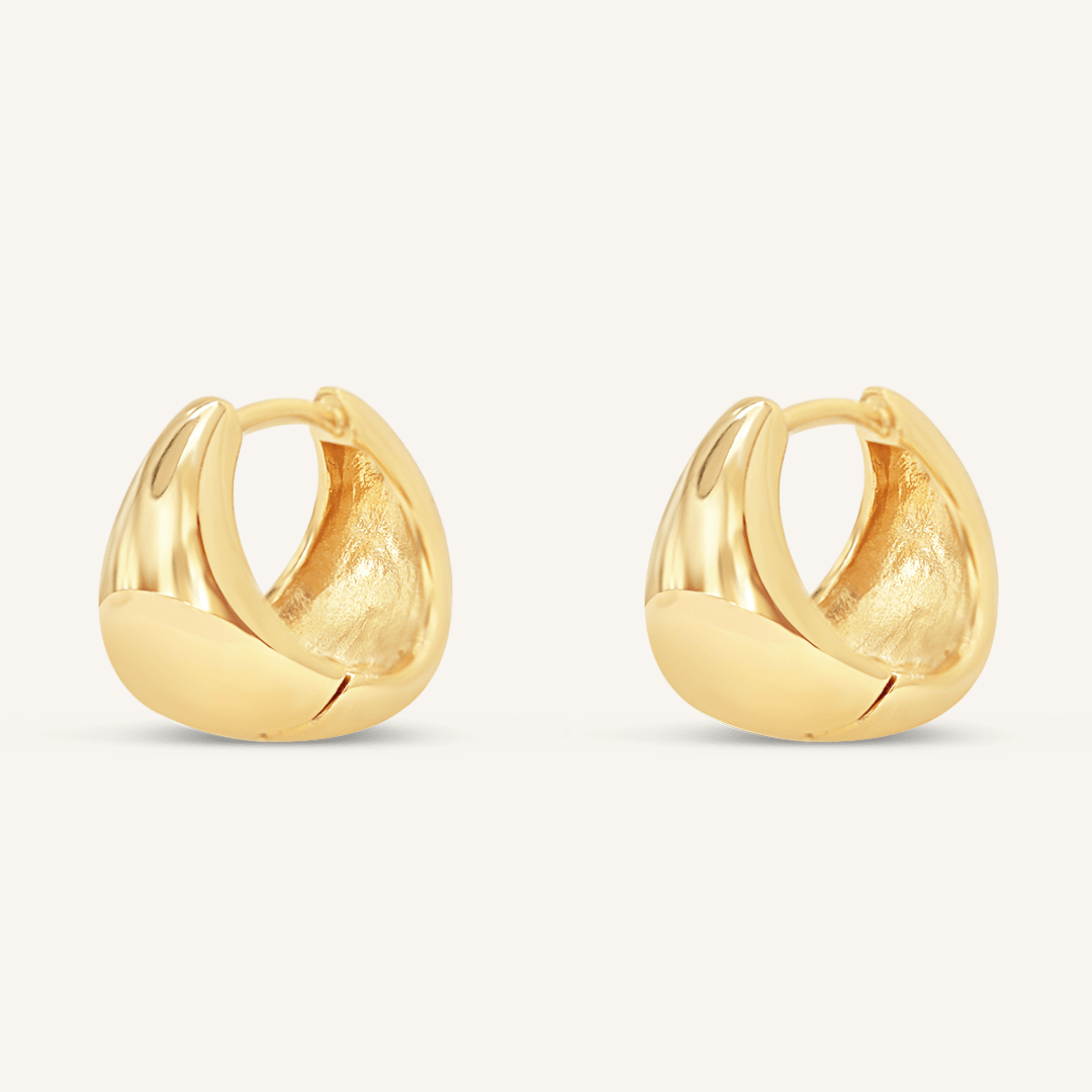 A pair of gold-colored huggie hoop earrings on a white background.