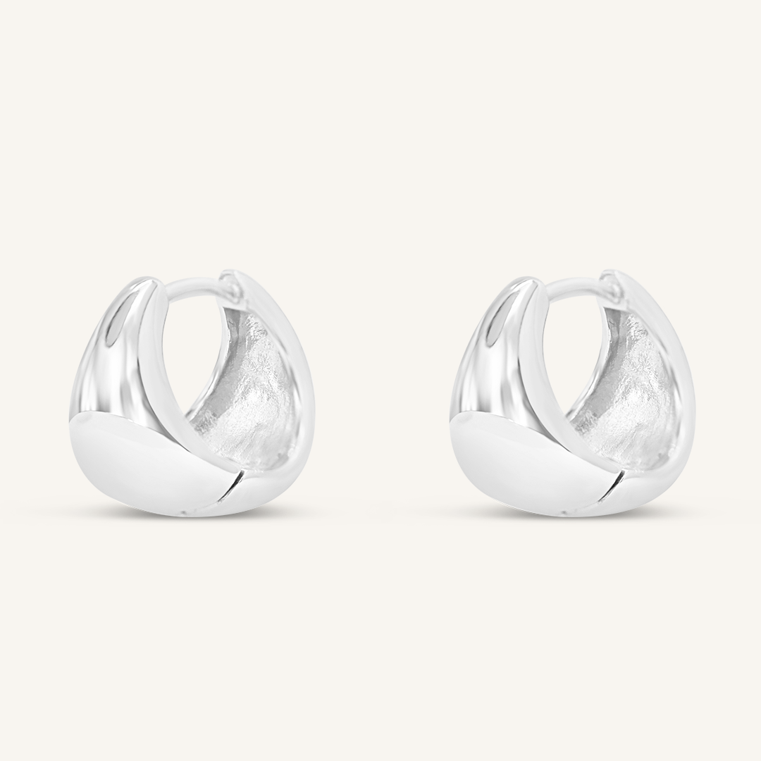 A pair of silver huggie hoop earrings on a white background.