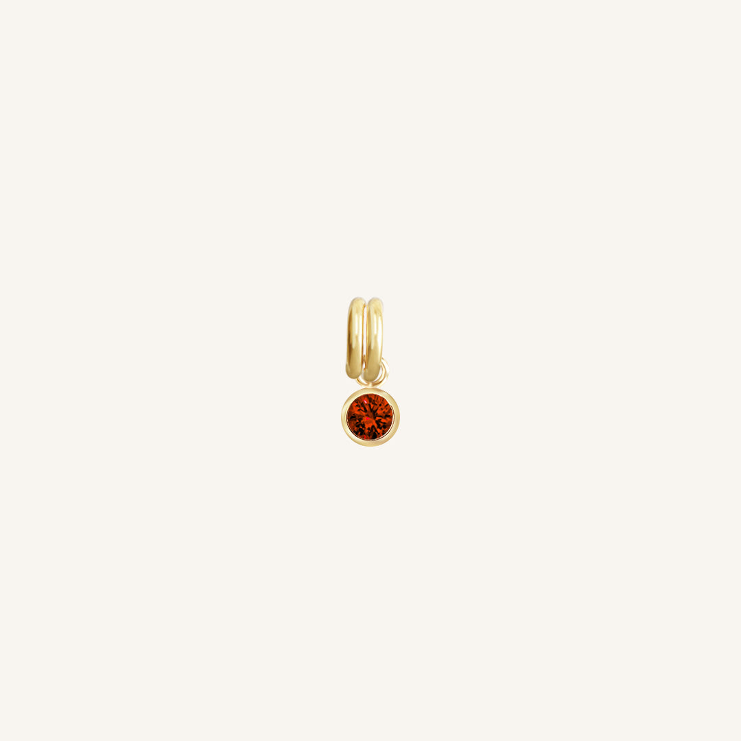 Round gold charm with bezel-set garnet cubic zirconia representing the January birthstone.