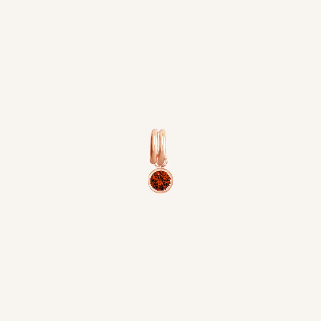 Round rose gold charm with bezel-set garnet cubic zirconia representing the January birthstone.