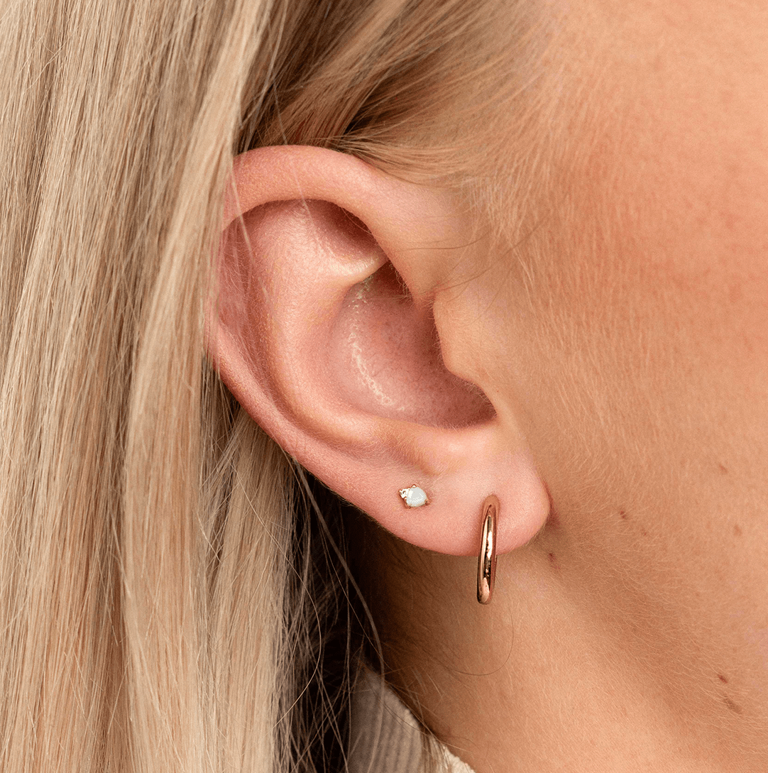 Close-up of an ear wearing a gold hoop earring and a small stud earring.