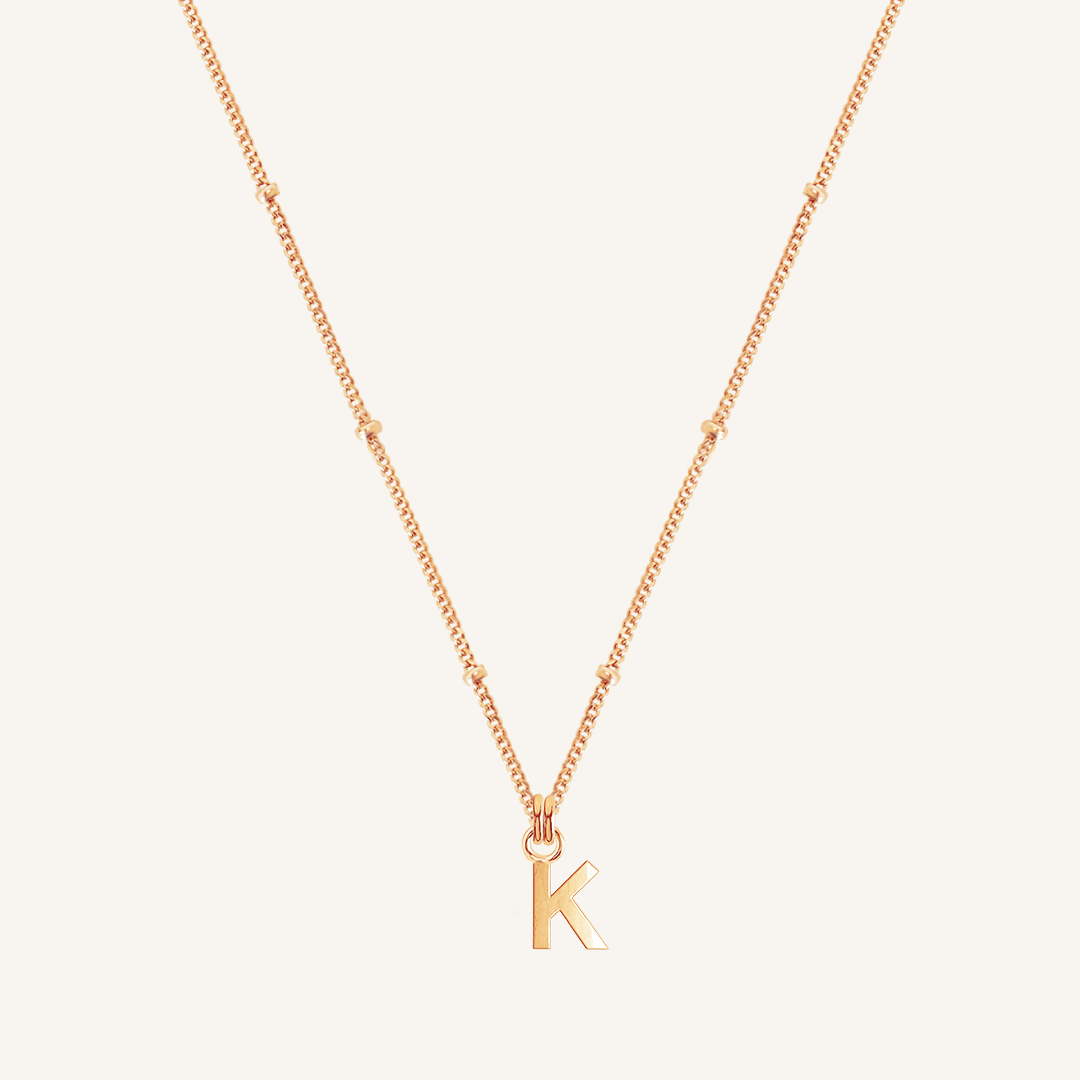 Rose gold necklace with a 'K' pendant on a light beige background