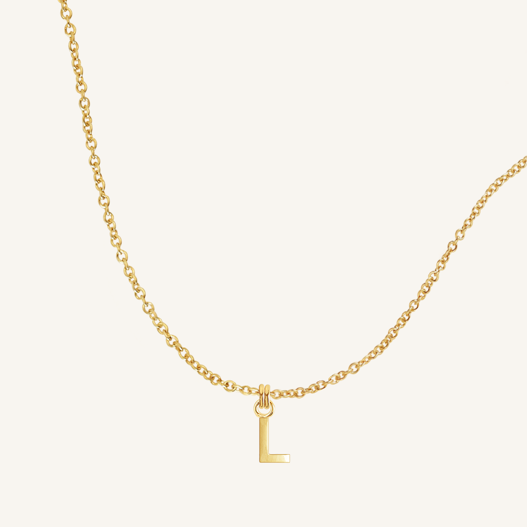 Gold necklace with a 'L' pendant on a light beige background