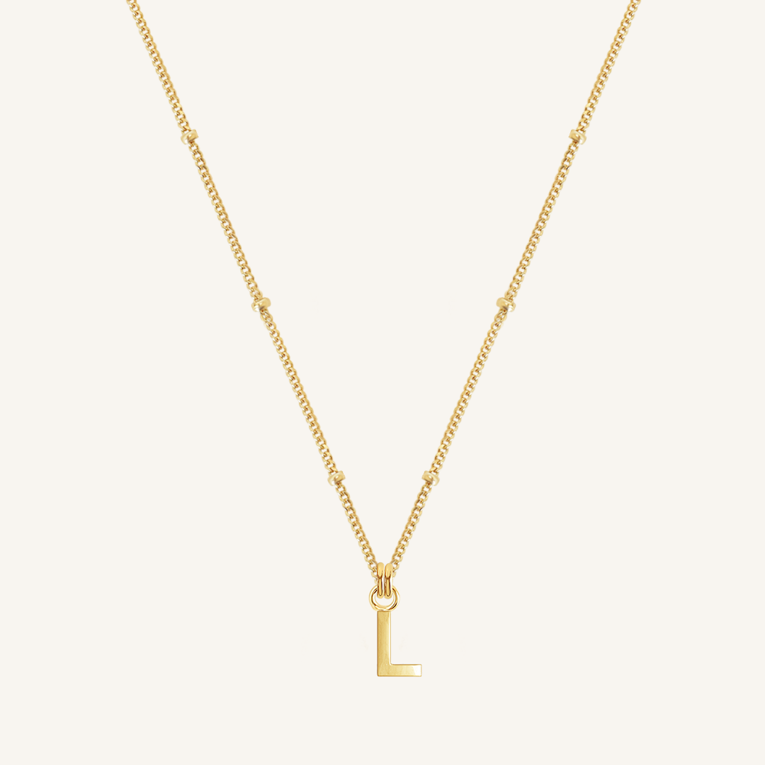 Gold necklace with a 'L' pendant on a light beige background