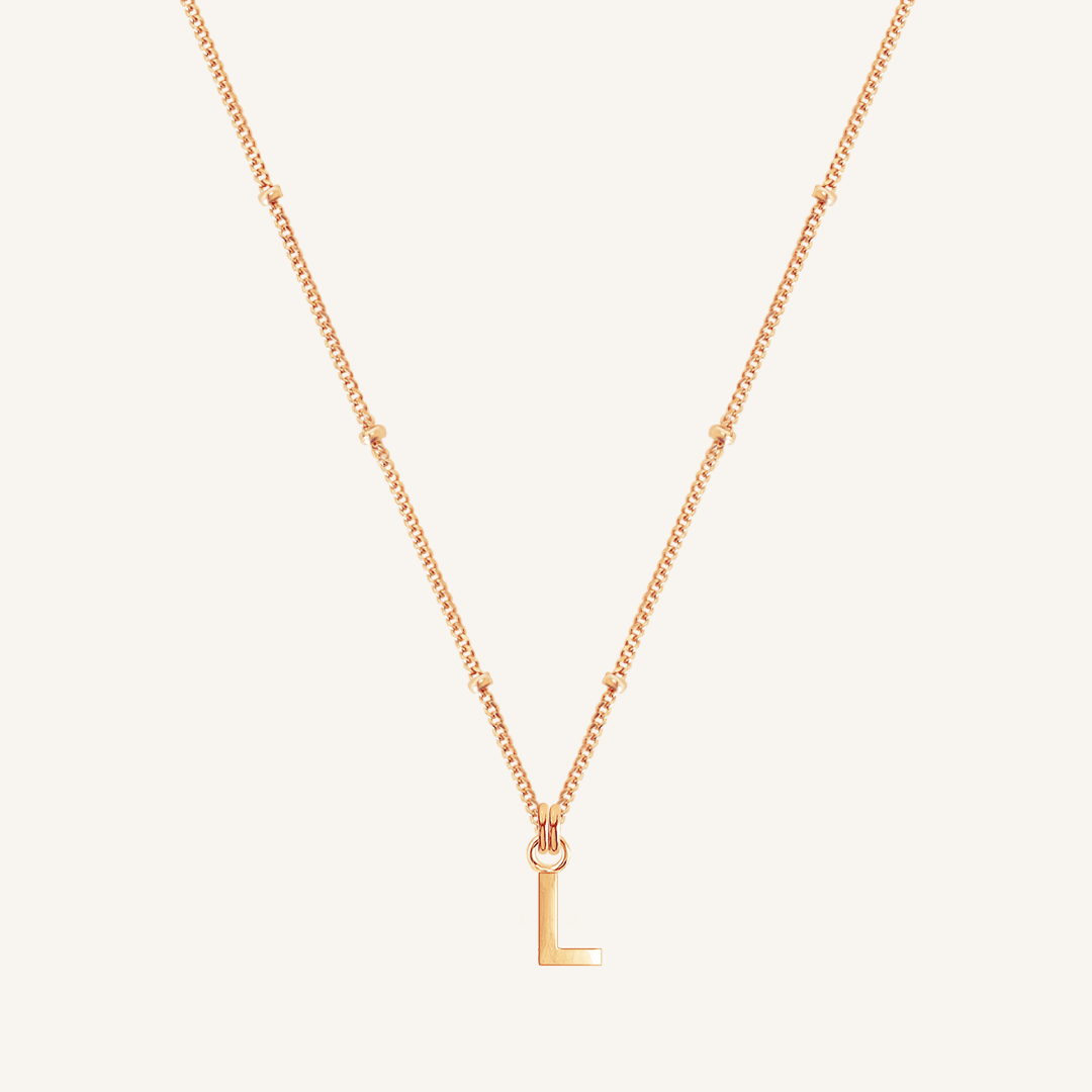 Rose gold necklace with a 'L' pendant on a light beige background