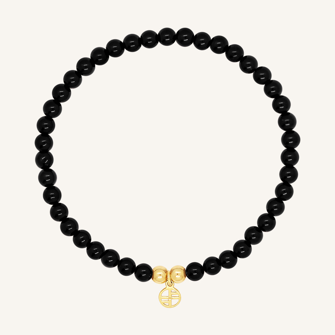 A black beaded bracelet made of black agate stones with a gold charm, displayed against a white background.