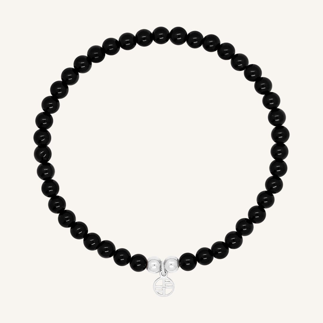 A black beaded bracelet made of black agate stones with a silver charm, displayed against a white background.