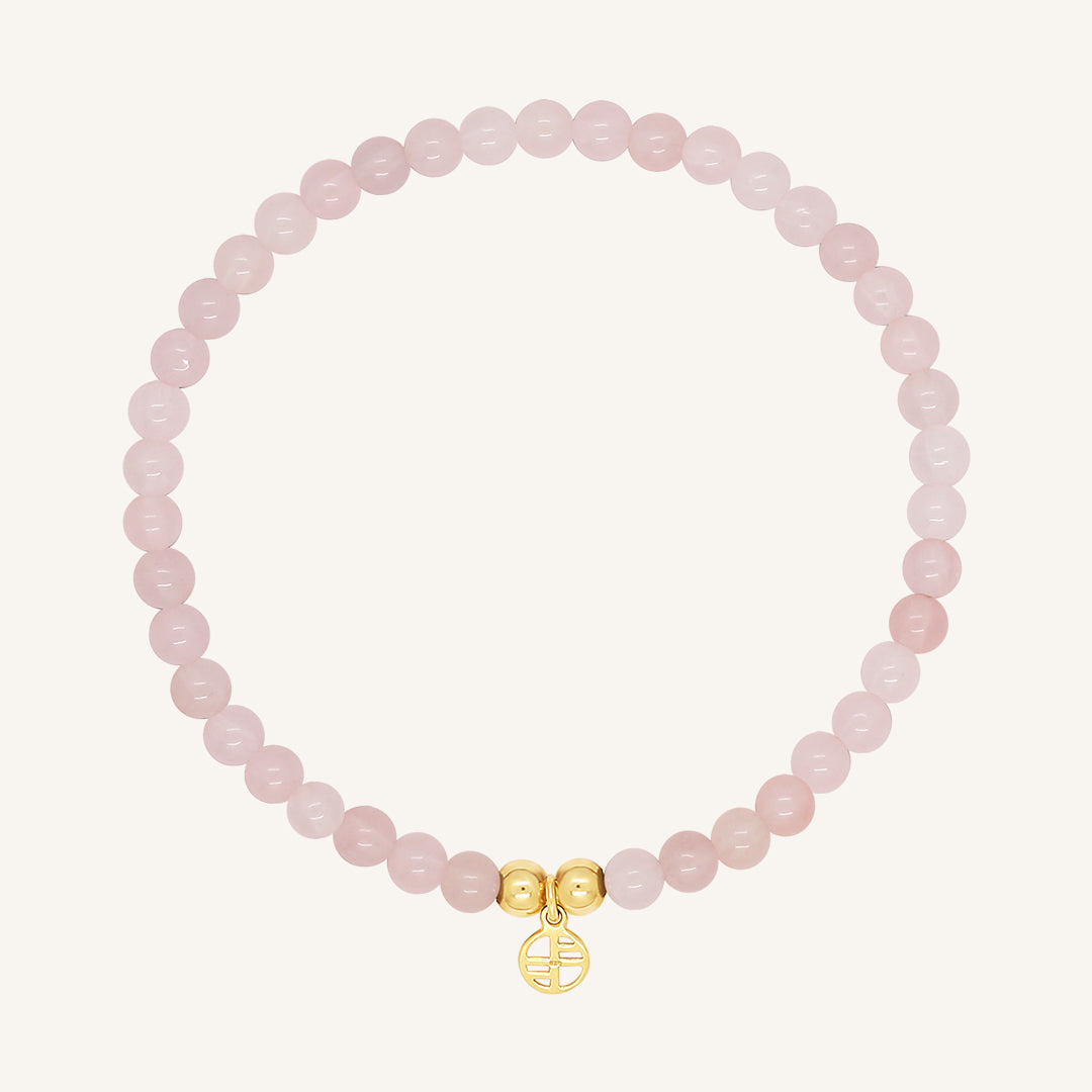 A rose quartz beaded bracelet with a gold charm, displayed against a white background.