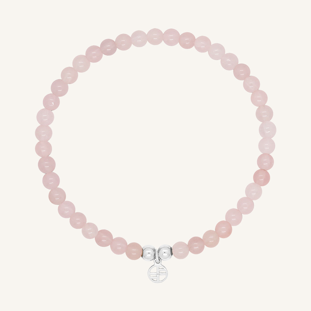 A rose quartz beaded bracelet with a silver charm, displayed against a white background.