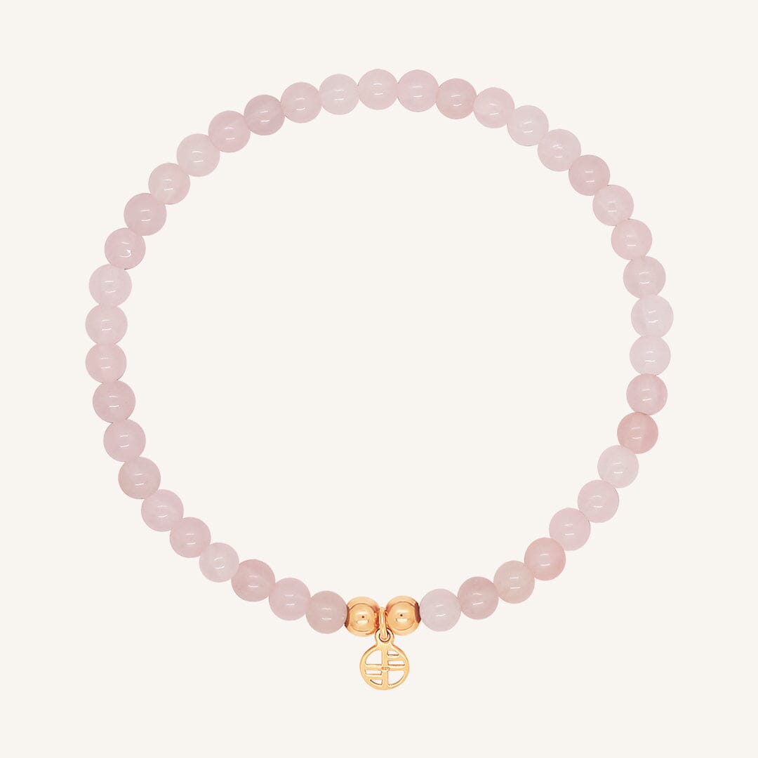 A rose quartz beaded bracelet with a rose charm, displayed against a white background.