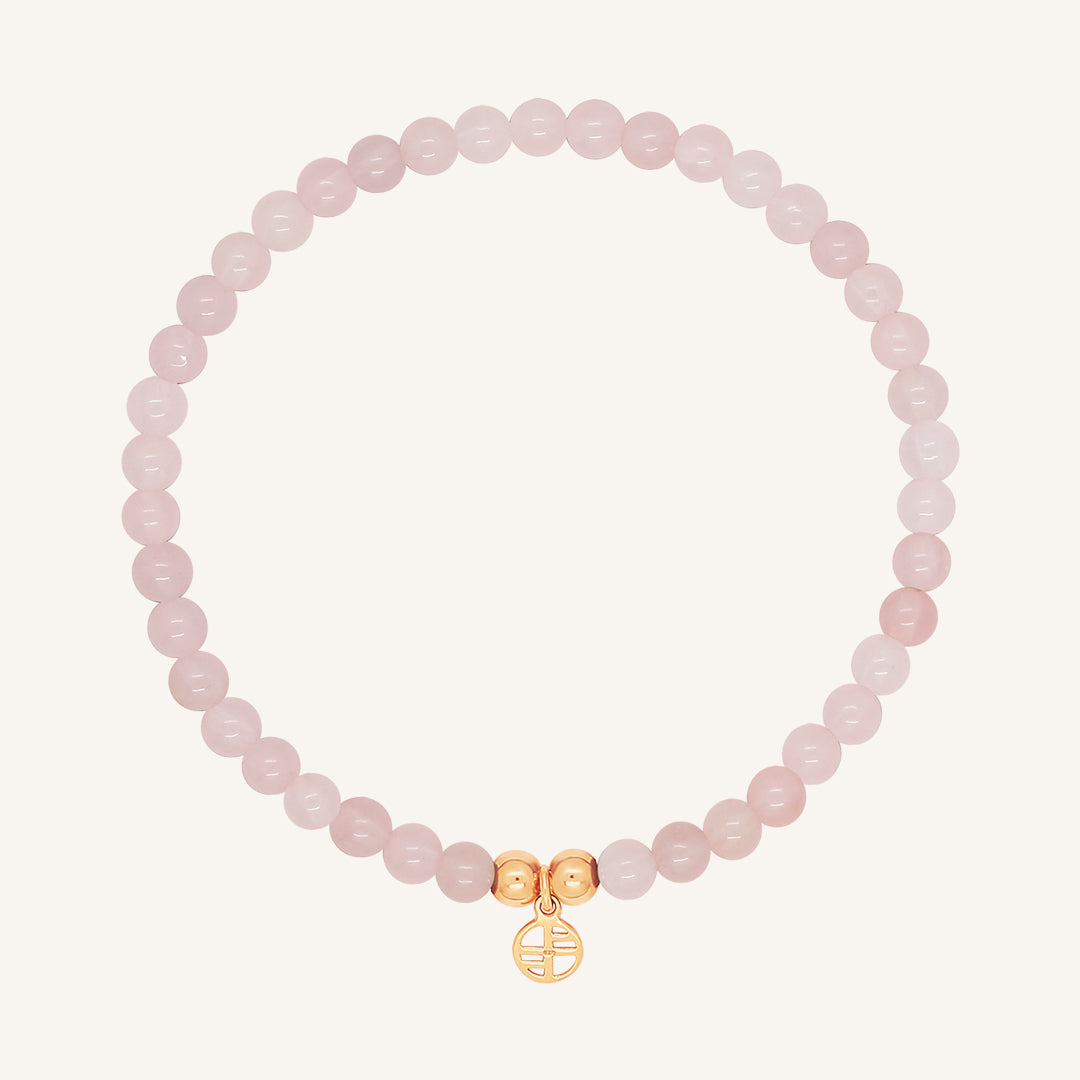 A rose quartz beaded bracelet with a rose charm, displayed against a white background.
