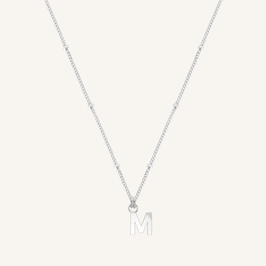 Silver necklace with a 'M' pendant on a light gray background