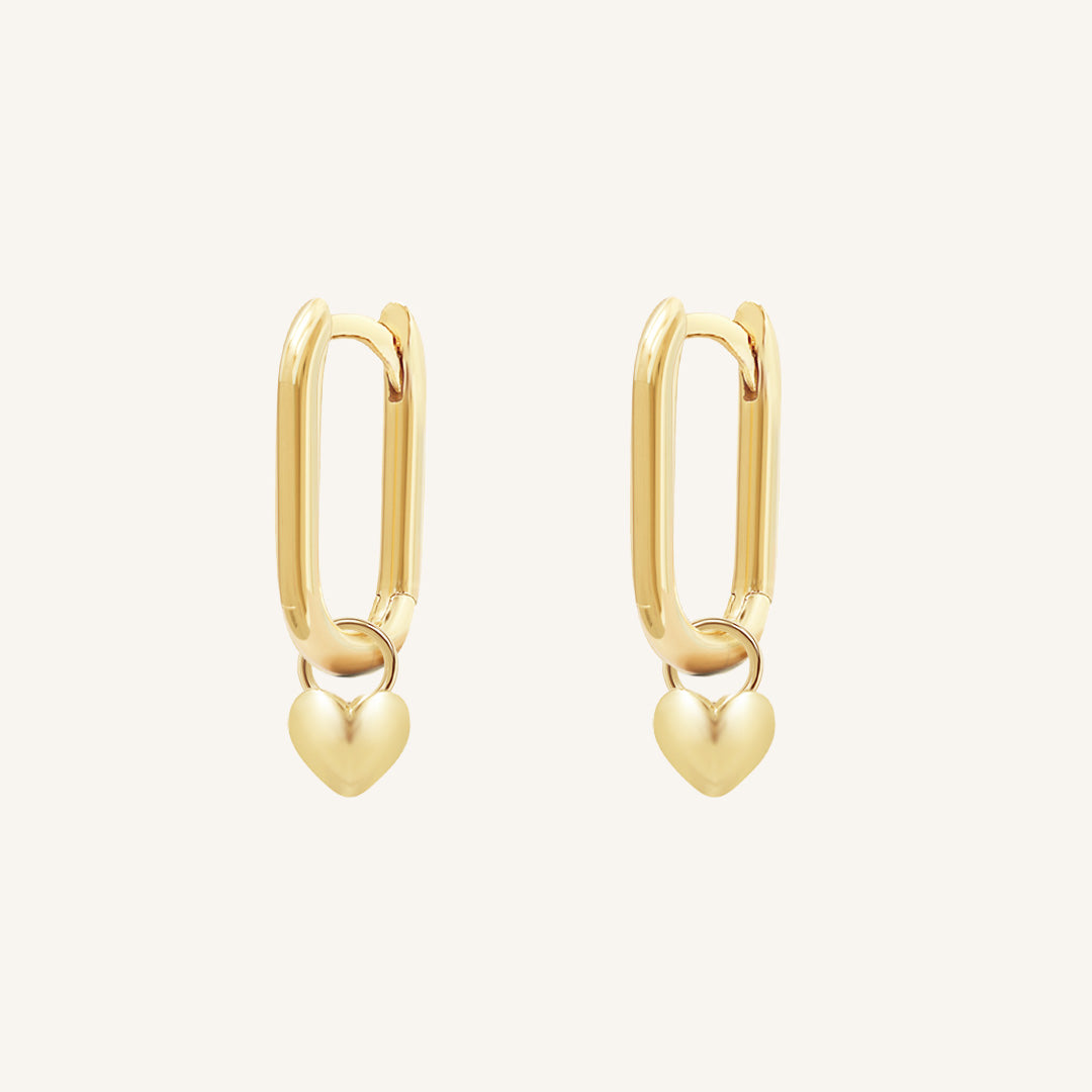 A pair of gold-tone hoop earrings with heart charms attached to them, displayed against a white background.